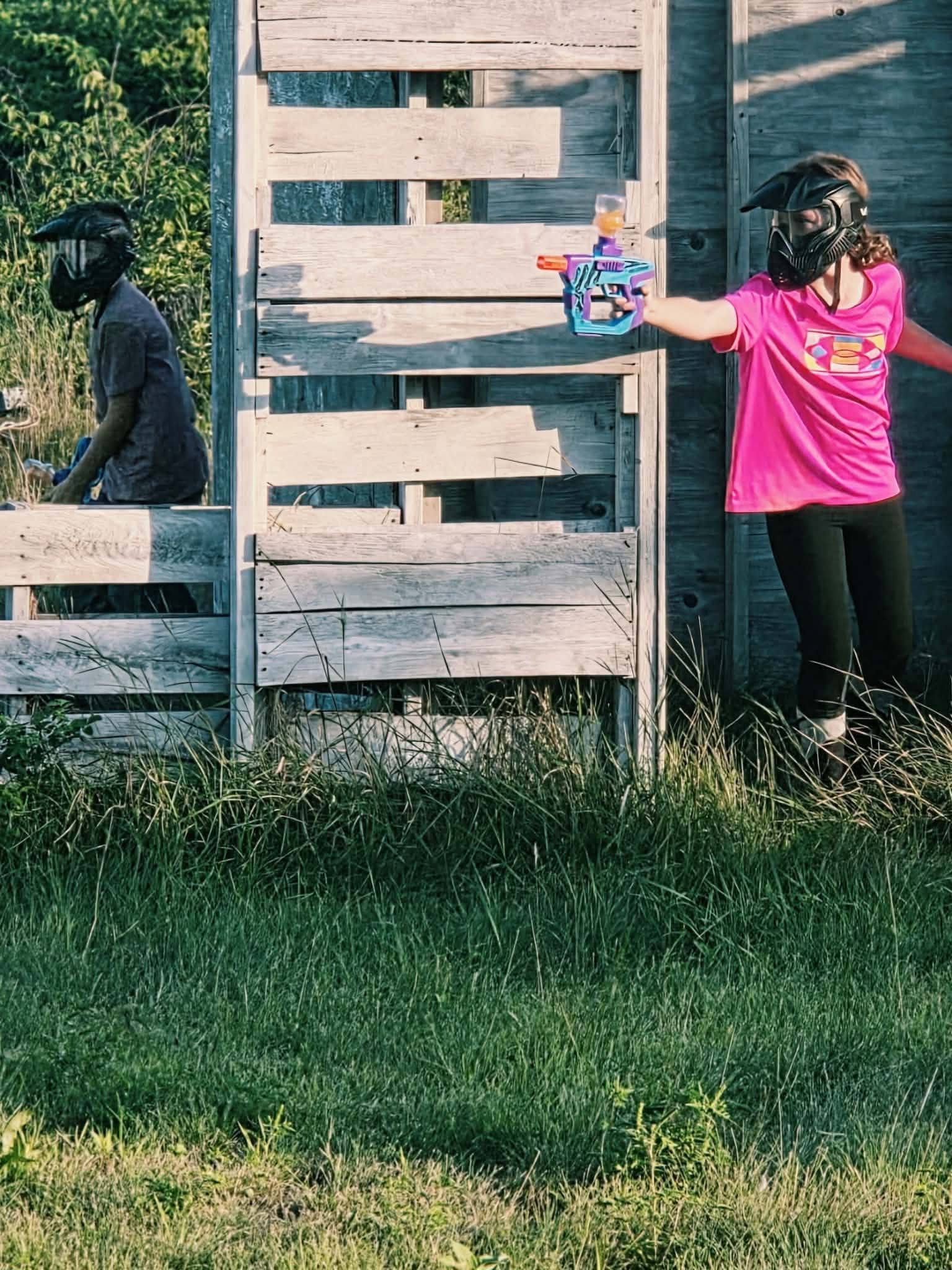 Young player aiming a gel blaster from behind wooden cover